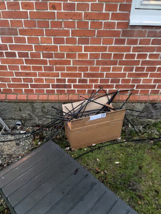 Kartong med tätningslister står lutad mot en röd tegelvägg utomhus.