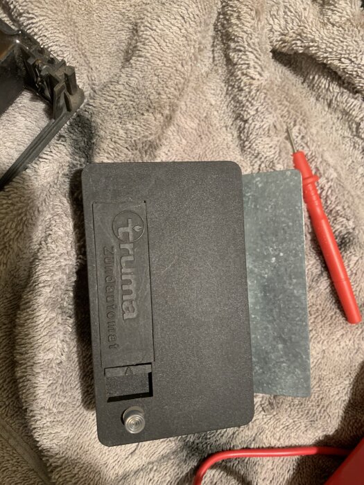 En svart Truma-tändare ligger på en grå handduk med rött verktyg i bakgrunden.