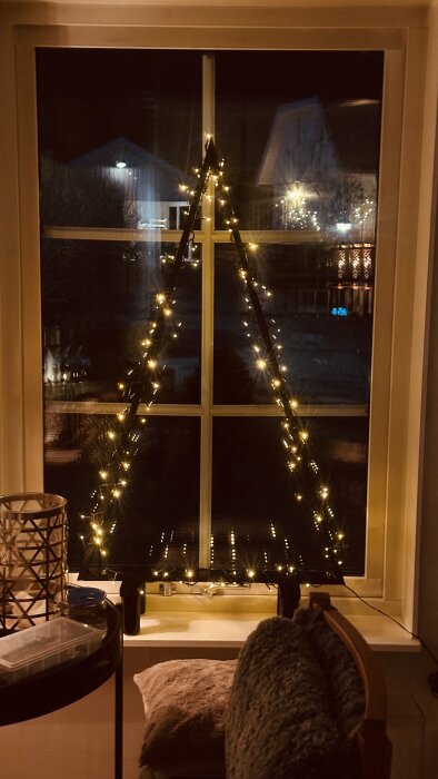 Återvunna spånskivor och sängben formar en trekant prydd med julbelysning i ett fönster.