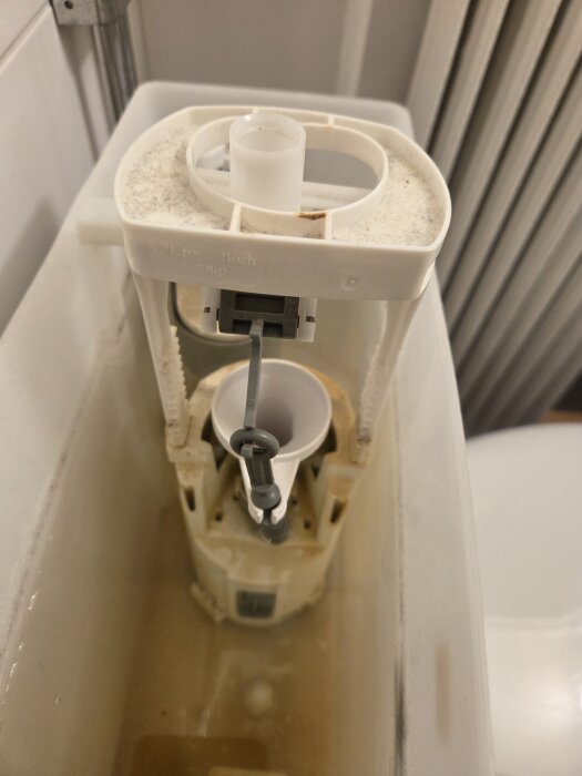 Närbild av en insida av Gustavsberg-toalettcisterner, visar spolmekanism med plast- och metallkomponenter delvis demonterade.