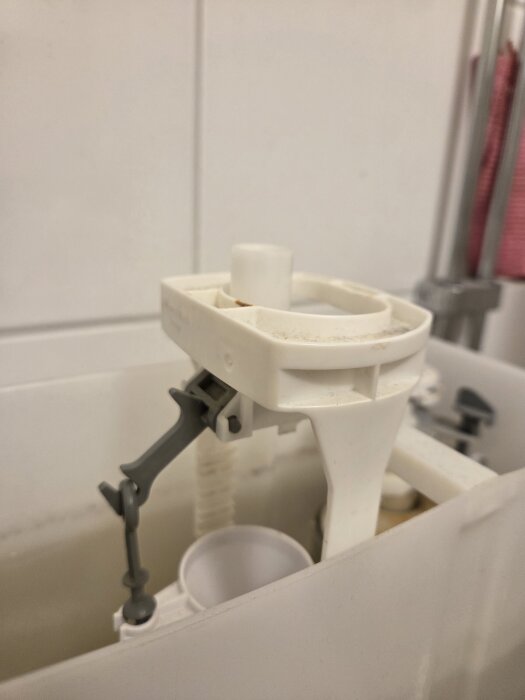 Närbild av toalettens inre mekanism med vit behållare och grå plastdetaljer, saknad fjäder tros orsaka spolproblem.