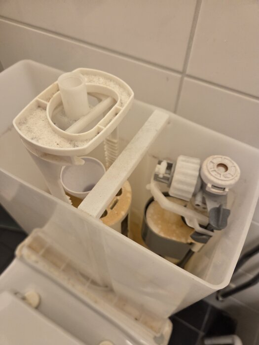 Inuti av en toalettcistern med synliga delar av spolningsmekanismen, inklusive en ventil och rör, delvis täckta med kalkavlagringar.