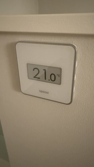 Termostat från Uponor visar 21 grader, installerad på vägg i ett rum.