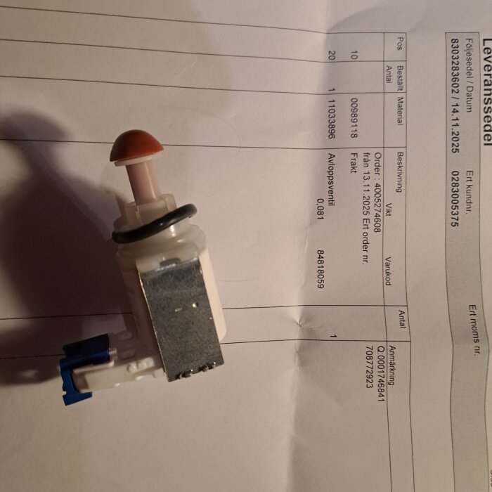 Vit och grå ventil ovanpå ett papper med beställningsinformation, vilket visar komponent beställd för en reparation.
