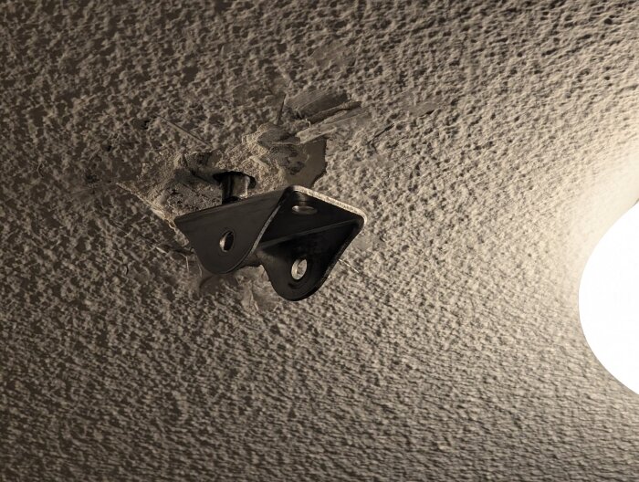 Monteringsanordning för gymnastikringar i betongtak, bult och metallbeslag synliga, delvis lossnat från det strukturerade taket.