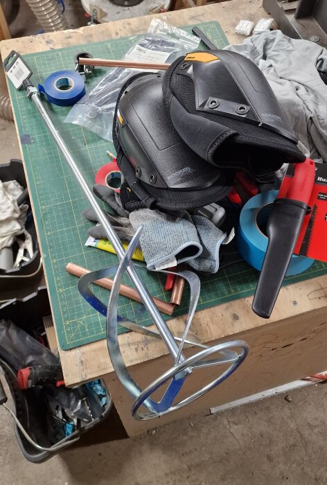 160 mm visp för blandning samt skyddsutrustning inklusive knäskydd ligger på ett arbetsbord i en verkstad.