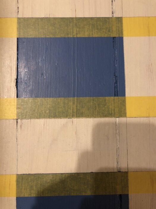 Blått golv målat med linoljefärg, inramat av gul tejp på en del omålat trä, med skuggor och ett slitet utseende.