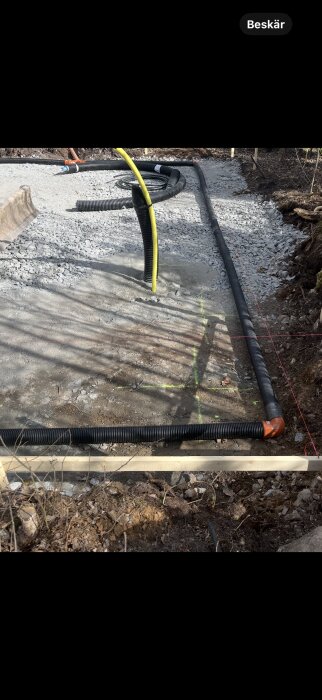 Gruslagd grund med dräneringsrör och makadam, inramad av trä och omgiven av jordig terräng.