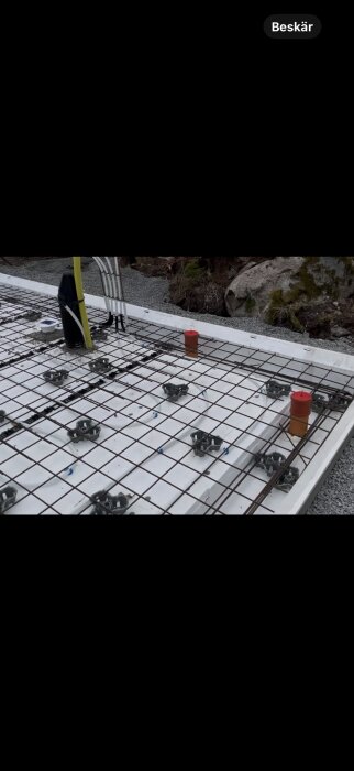 Armeringsjärn placerade på cellplast och makadam, med rör och kabelgenomdragningar för ett byggprojekt.