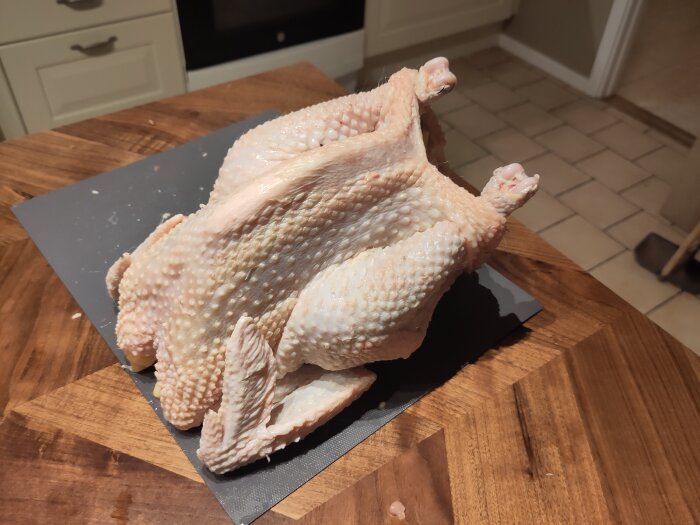 Rå plockad kyckling på en skärbräda i ett kök.
