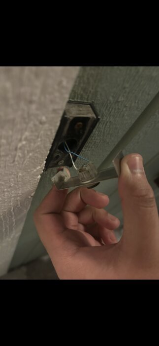 Person håller i en dörrklocksknapp med synliga kablar och en monterad platta.
