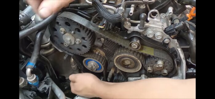 Motor med exponerad remdrivning från en Golf Variant TDI. En hand justerar delar nära remmen.