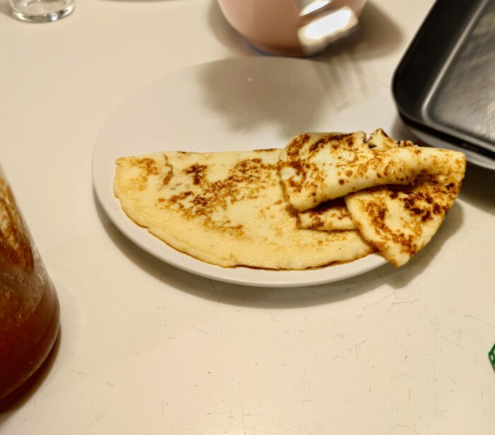 Tallrik med tre pannkakor, varav två är vikta, på ett vitt bord.