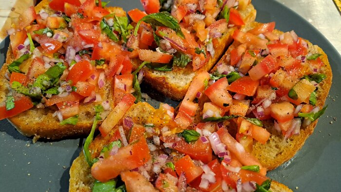 Bruschetta med tomat, rödlök och basilika på en grå tallrik.