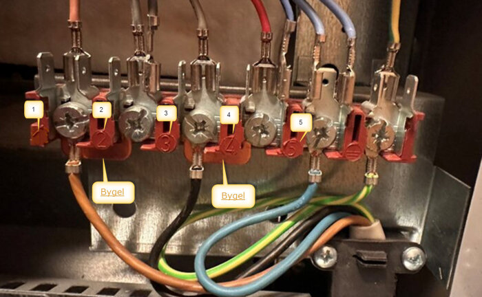 Elektrisk kopplingsplint med nummererade anslutningar och byglar mellan 1-2 och 3-4, omgivna av färgade kablar.