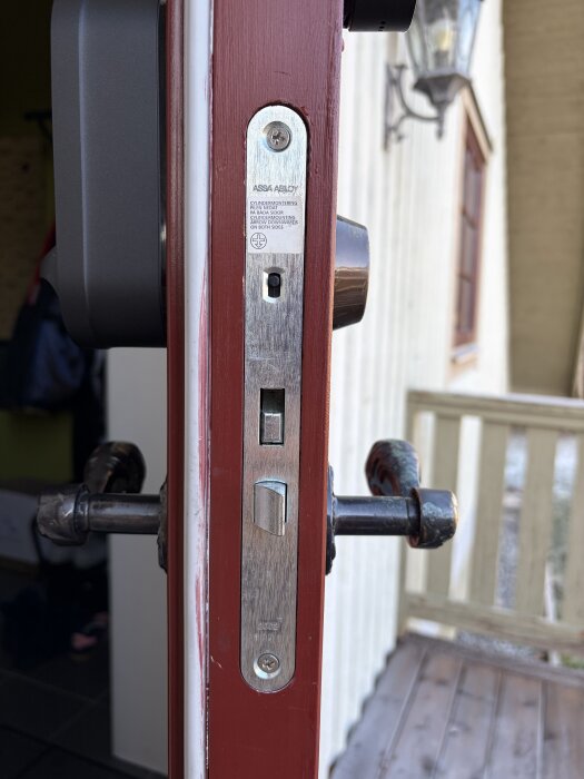 Rött dörrfoder med monterat ASSA 2002 lås och 1487-11 slutbleck, svart Aqara U200 syns i bakgrunden.