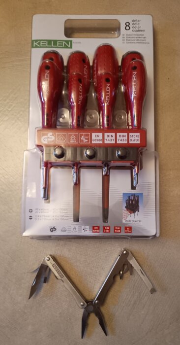 Förpackning med röda Kellen-skruvmejslar och ett öppnat Kellen-multiverktyg på en beige yta.