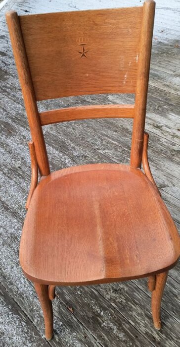 Stol av trä i retrodesign med Televerkets emblem inristat i ryggstödet, stående på en sliten träaltan.