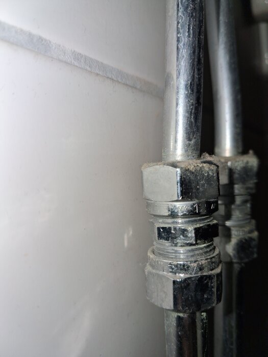 Närbild på två metallrörsanslutningar i ett badrum med märkningen "vattette 12" synlig på muttern.