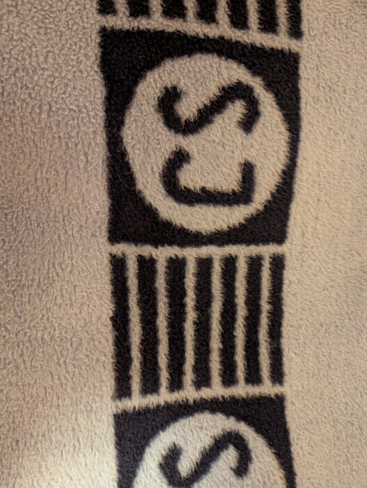 En svartvit handduk med mönster av bokstaven "S" i en cirkel och randig design.