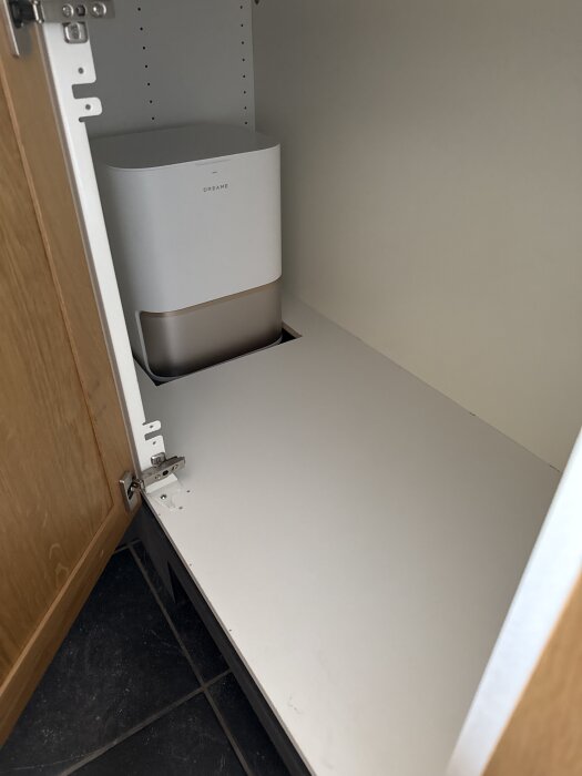 Dreame basstation inbyggd i ett kökskåp med ett hål i tröskeln för dolda dammsugaraktiviteter, sedd ovanifrån.