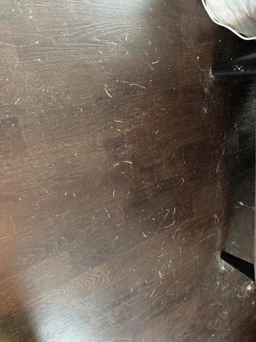 Repor på mörkt trägolv orsakade av dubbade skor. Golvet visar ytliga skador som fångar ljus. Fråga om hårdvax för reparation diskuteras.