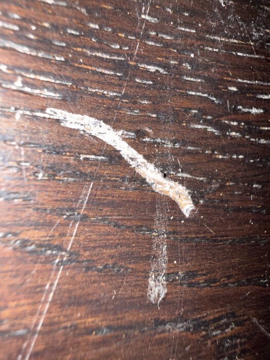 Repor och skador på en mörk trägolvyta, nära fotograferade.