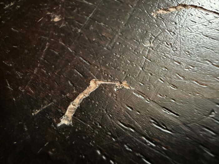 Repor och skador på ett mörkt trägolv, troligen orsakade av dubbade skor. Frågan handlar om reparation med hjälp av hårdvax.