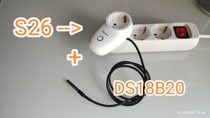 Sonoff S26 smart plug och DS18B20 temperatursensor på ett skrivbord, ansluten strömuttag i bakgrunden.