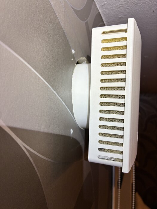 Ett luftventilationsrör sticker ut från en vägg med en vit plastikventil inte helt anpassad mot väggen.