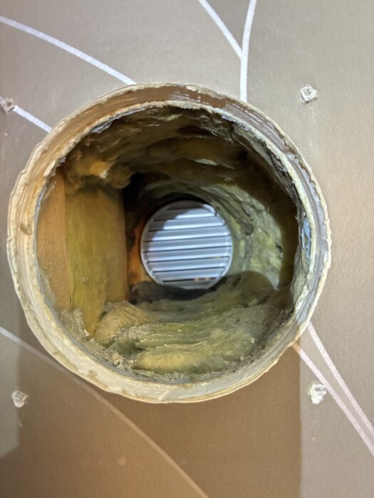 Öppen väggventil med metallrör och isolering visad från insidan, mot ett galler utanför.