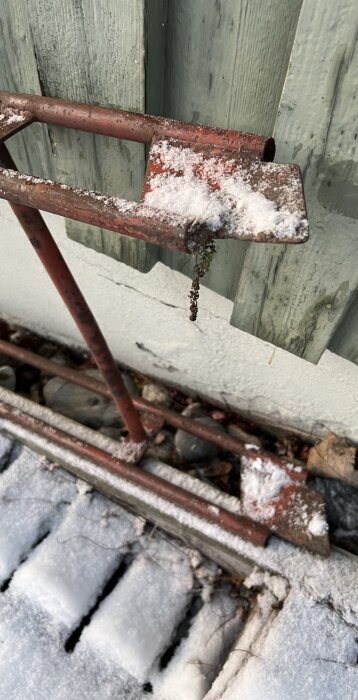 Gammal röd stege med snö på sprucken garagedörr, stående på skottad isig betongyta. Potentiell säkerhetsrisk vintertid.