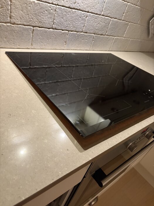 Induktionshäll på kvartskomposit-bänkskiva med tegelvägg i bakgrunden. Hällen är inte helt nedsänkt i bänkskivan.