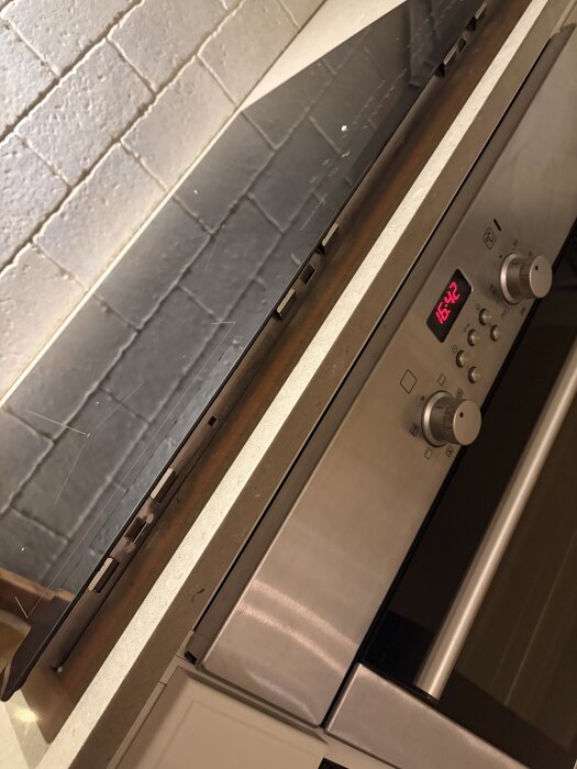 Inbyggd spis med digital klocka och vred på en köksbänk, fotograferad framifrån.