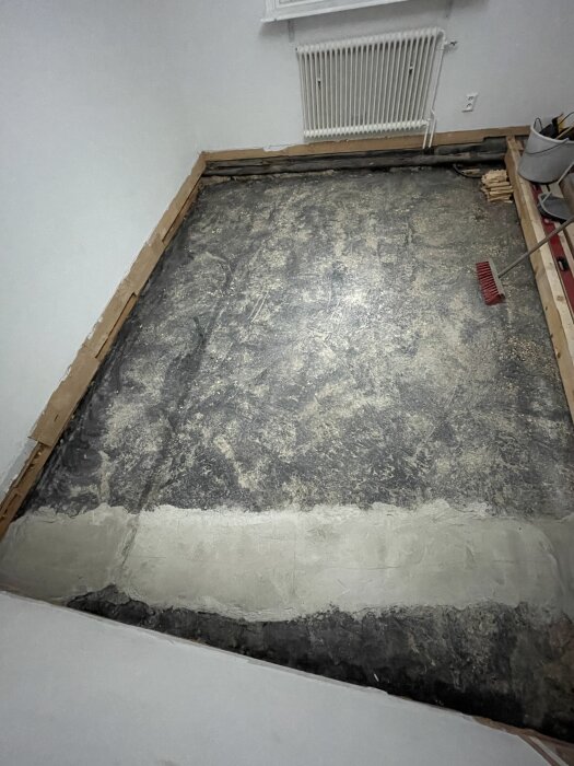 Oisolerad betongplatta från 1958 i en bostad med träkarmar, en radiator på väggen och en kvast bredvid.
