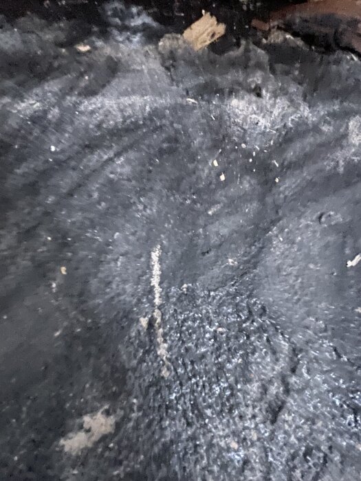 En närbild av en betongplatta med mörk yta, troligen behandlad med en spärrfärg för fuktskydd, från en renoveringsdiskussion.