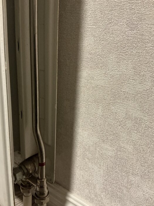 Rörkopplingar och anslutningar vid ett vattenburet element mot tapetbeklädd vägg.