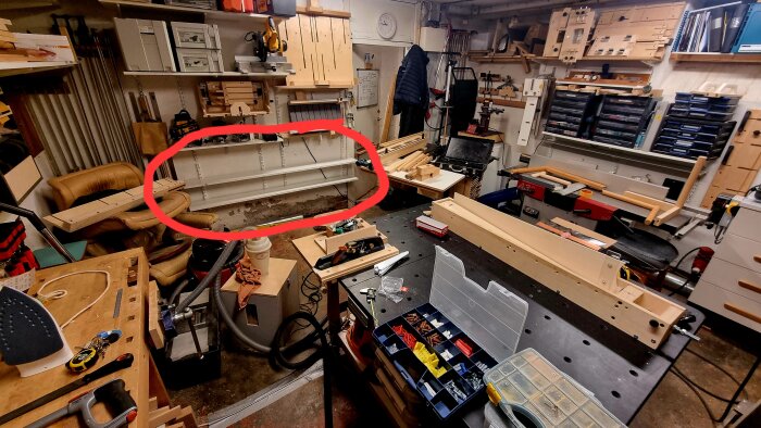 Verkstad med två nyligen uppsatta hyllor i hålrummet bakom en såg, används för att förvara sällananvända jiggar. Redskap och material synliga.