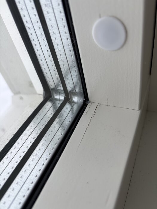 Närrbild av ett fönster med spruckna karmar och kondens längs med glaset, upplevt i ett nybyggt hus vid kallt väder.