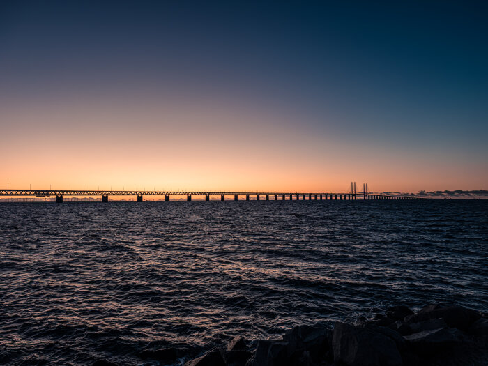 Bro i solnedgång över hav, med klar himmel och vågor i förgrunden.