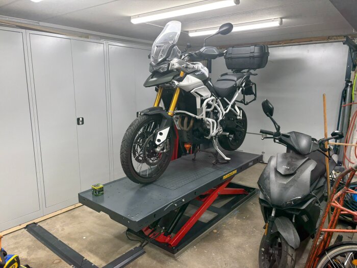 Motorcykel på en lyft i garage för service med ny kedja och bromsbelägg, verktyg och annan utrustning syns i bakgrunden.