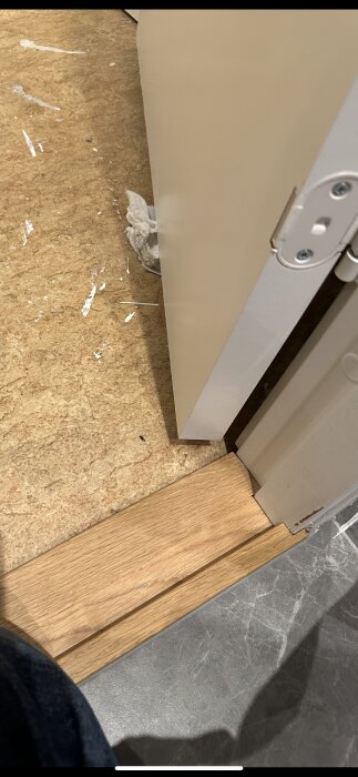 Badrumströskel med borttagen trälist och fuktansamling, visar skadad fog och silikon nära vägghängd toalett.