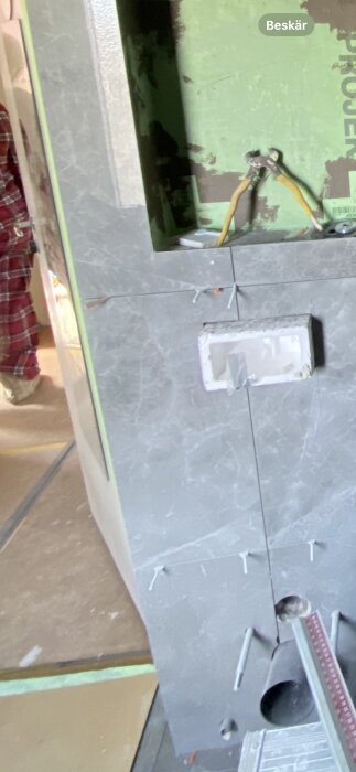 En vägg under renovering med plattor och fogning synlig. Verktyg och material visas, indikerar problem med tätskikt bakom kaklet.