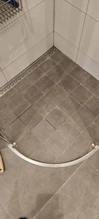 En dusch med grå kakel och synlig metallbrunn, visar på fuktproblem med mörkare fogar och antydan till läckage vid trasiga fogar.