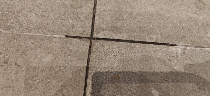 Närbild på kakelfogar i ett badrum, några fogar ser blöta och mörklagda ut, möjligen på grund av vattenläckage eller fuktproblem.