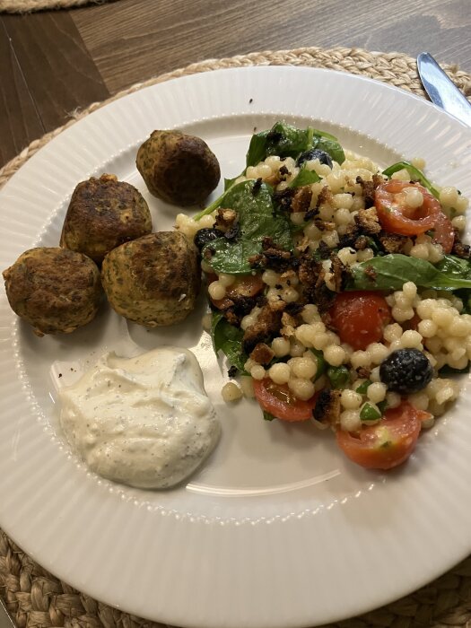 Tallrik med marockanska fiskbullar, pärlcouscous med körsbärstomater, svarta oliver, spenat, citronsaft och en klick yoghurtsås med mynta.