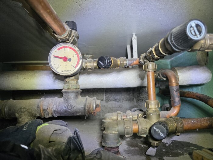 Tryckmätare och rörkopplingar i pannrum, visar tryck på 2 bar. Kopplingar och ventiler synliga, relaterat till vattenläckageproblem.