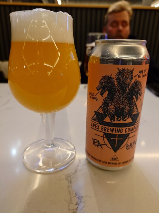 Ett glas med skummande IPA och en burk Apex Brewing Company IPA på ett bord.