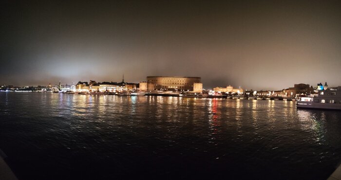 Upplyst slott och riksdagshus vid vattnet under natthimmel, med speglingar i vattnet.