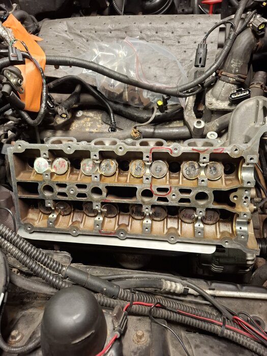 En närbild på en motor med avmonterat topplock, visande ventilsäten och den inre motorstrukturen, omgiven av kablar och verktyg.